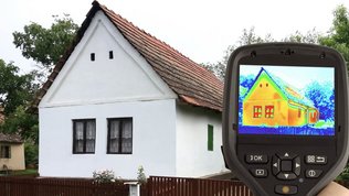 Ein Handgerät zeigt ein Wärmebild eines Hauses mit einem roten Dach und weißen Wänden, umgeben von Bäumen und einem Garten.