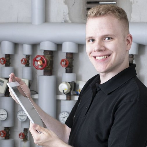 Ein Anlagenmechaniker vor einer Heizungsanlage mit einem Tablet